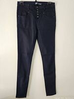 Front view of the pants showing the button-fly closure, front pockets, and overall slim silhouette in black fabric.