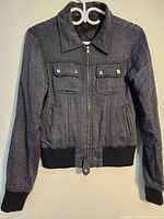 Front view of the dark grey woman's jacket with collar, zipper closure, and double chest pockets with buttons.