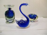 Three art glass pieces including swan, layered glass sculpture, and small abstract bowl shown together