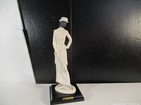Front view of white porcelain Armani statue on black base against black background.
