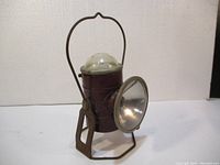 Front angle view of vintage Ecolite railroad brakeman's lamp showing cylindrical maroon metal body, reflective side lens, and rusted metal base support.