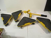 Four yellow and black triangular furniture dollies and one yellow furniture lifter on white background