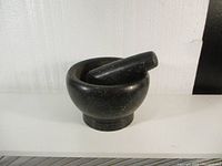 View of black stone mortar with pestle resting inside, showing shape and finish