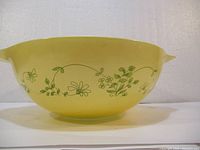 Side view of yellow Pyrex mixing bowl with green floral pattern on exterior.