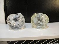 Set of two snowball-shaped textured glass candle holders on a black and white surface