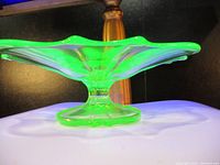 Side view of the green uranium glass dish showing the pedestal base and ruffled edge glowing under UV light.