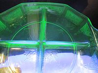 Top view showing the bright green fluorescence of the uranium glass dish under UV light, divided into four sections with etched decorative patterns.