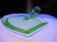 Uranium glass serving dish under UV light showing bright green fluorescence and the shape and handle of the dish.