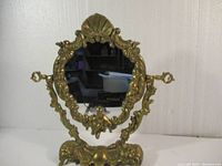 Front view of the vintage brass tilting mirror showing overall shape and intricate scrollwork.