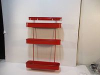 Front view of the vintage red metal kitchen wall shelf showing all three tray levels and the wall mounting bracket.