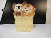 Front and angled view of vintage ceramic cookie jar showing two animals (koala and fox) sitting inside a bag.
