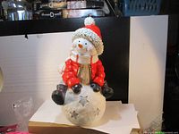 Front view of the full snowman figurine showing the red coat, white scarf, and snowball base with star cutouts.