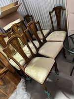 Set of six dining chairs arranged in two rows showing wooden backs with floral inlay and cream patterned upholstery on seats and legs.