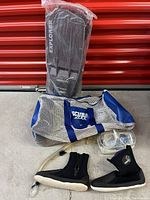 Photo shows a set of snorkeling gear including black Explorer brand flippers in packaging, black neoprene water booties with zipper, clear goggles, snorkel, and a blue and white mesh bag with Scubapro branding on a concrete floor.