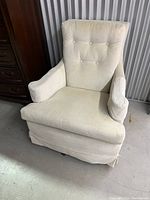 Cream/white fabric reclining rocking swivel chair showing front view with cushioned armrests and button tufted backrest, on a concrete floor.