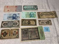 Photo of 12 foreign currency notes laid out flat on light patterned fabric showing different countries and denominations.