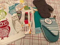 Overview of all items in lot showing kitchen towels, mitts, and potholder on checkered surface.