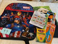 Full view of Marvel backpack with superheroes: Captain America, Iron Man, Spiderman, Black Panther, Thor, Rocket Raccoon and Captain Marvel. Included in front is Crayola crayons, Fiskars scissors, and dot gross motor stickers with vehicles.