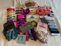 Photo of a variety of new, colorful hair accessories including clips, scrunchies, hair coils, and elastic bands on a white blanket.