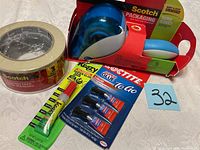Photo showing all items in the lot including 3 rolls masking tape, packing tape with blue dispenser, Krazy super glue and Loctite super glue pack