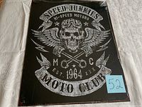 Front view of black tin sign with skull and crossed pistons design and 'Speed Junkies Moto Club' text, sealed in plastic with torn section on the bottom back.