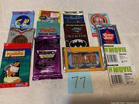 Photo showing 11 unopened non-sports collectible card packs from various franchises and themes arranged on a surface with a lot number 77 card in front.