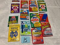 Top view of 16 unopened sports card packs arranged in a grid on white fabric surface.