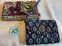 Photo of two Vera Bradley wallets, one multicolored floral and one navy blue teardrop pattern, showing quilted fabric and metal turn-lock closures.