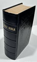 Closed view of the Holy Bible showing thick black leather rebound cover with embossed design and gold stamped spine title.