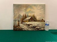 Full view of oil on canvas painting showing winter cabin landscape and snow-covered path, height approximately equal to a water bottle beside it for scale.