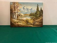 Full view of the signed landscape oil painting showing the entire scenery with cabin, trees, lake and mountains.