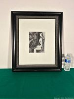 Full view of framed lithograph on green table beside a water bottle