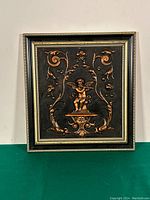 Full view of framed repousse copper artwork featuring cherub and floral scroll motifs.