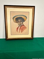 Framed print leaning against a white wall on a green surface, showing full artwork and frame.