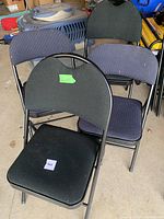 Four cloth-covered folding chairs arranged in a garage setting, two black and two dark blue upholstery, metal frames visible.