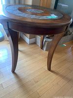 Side view of the round wood accent table showing curved legs and wooden frame.
