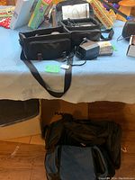 Photo showing two black camera bags along with battery charger and battery/film box on table