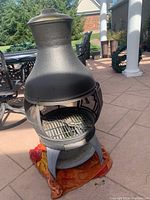 Full view of the chiminea showing its overall shape and structure on a patio with an orange towel underneath.