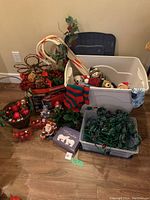 Photo showing assorted Christmas decorations including small teddy bears dressed in Christmas attire, decorative candy cane, basket with Christmas balls, assorted small holiday figurines, and a large white storage bin containing some of the items.