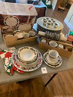 Photo showing full assortment of Christmas themed dinnerware including plates, bowls, teacups, saucers, chargers, and napkin rings along with holiday cloth napkins.