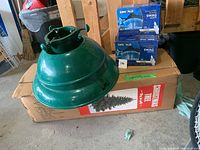 Green metal Christmas tree stand on top of large box labeled 'Christmas Tree'.