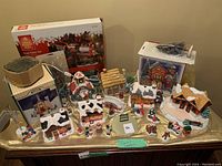 Wide view of Christmas village buildings including houses, figurines and boxed tree train set.