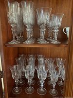 Image showing two shelves of various crystal glasses including tall wine and champagne glasses and shorter liquor glasses with intricate cut patterns.