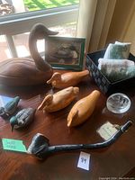 Overview of large wooden duck, smaller wooden ducks, ceramic ducks, hand towels in basket, glass paperweight, and black pipe