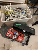 Overview photo showing beige storage bin filled with extension cords, cables, and battery organizer, with black toolbox containing hardware items in front