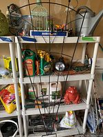 Photo showing metal plant trellis in front of shelving unit with garden chemicals and ceramic frog decoration on shelves.