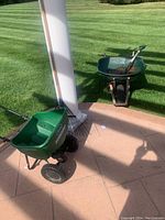 Set of garden tools including wheelbarrow, shovel, spreader, and rake on outdoor patio and lawn area.