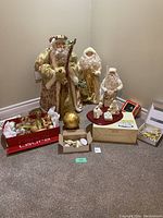 Full view of gold-themed Christmas decor including three Santa figurines and assorted gold ornaments arranged on floor.