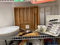 Photo showing bamboo cutlery tray with compartments, stacked white soup bowls, ceramic dishes with botanical patterns, spreaders, and serving utensils.