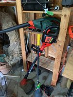 Full view of the lot showing Black & Decker string trimmer with yellow handle and Greenworks leaf blower resting vertically in garage shelving area.